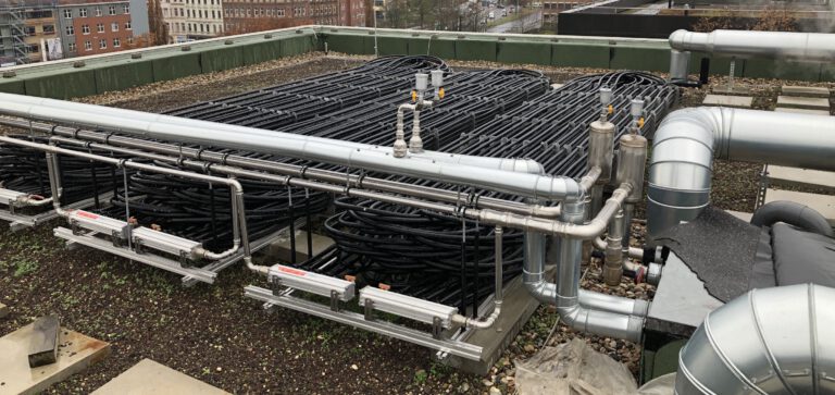 Großflächige Rohrleitungsinstallation mit Verteilern auf einem Gebäudedach im urbanen Umfeld